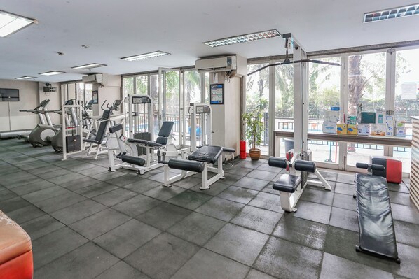 A gym with various exercise equipment, large windows, and a view of palm trees outside.