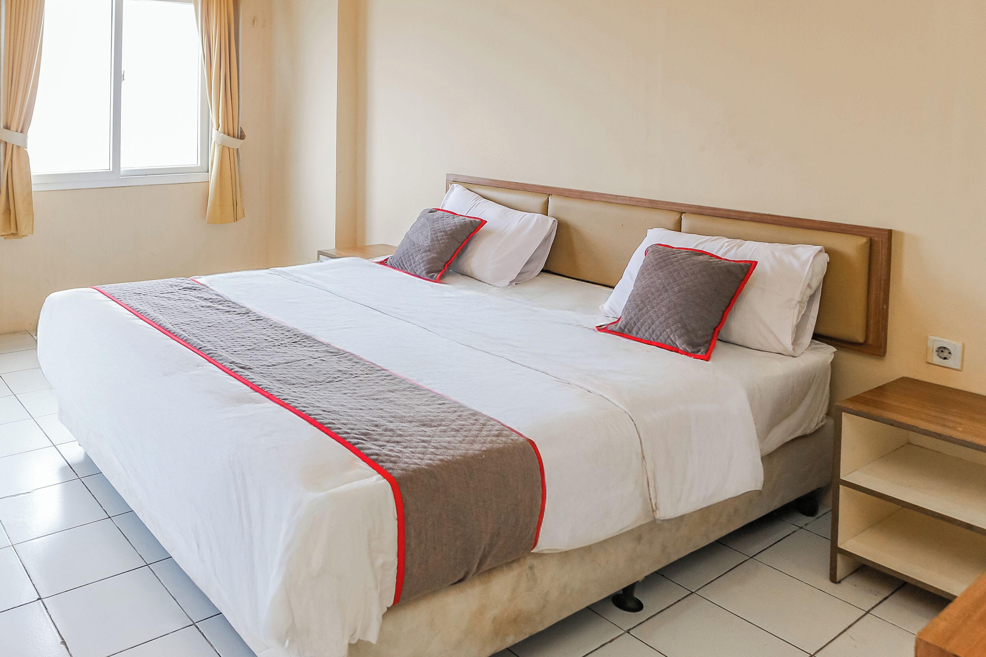Een opgemaakt bed met een houten hoofdbord, een nachtkastje en een raam met gordijnen.