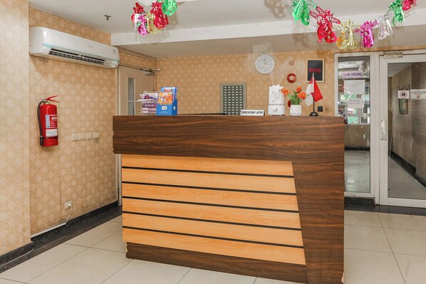 A reception desk with a wooden finish, a fire extinguisher, a clock, and a 'No Smoking' sign. - Capital O 94796 Apartment Mutiara Bekasi (Bekasi)