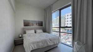 A modern bedroom with a large bed, a nightstand, a window with a view of city buildings, and a hanging chair. - Luxury 1-bedroom fully furnished Lifeline apartment  (Abu Dhabi)