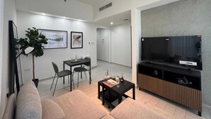 A modern living room with a flat-screen TV, a dining area with chairs, a coffee table, and a sofa. - Luxury 1-bedroom fully furnished Lifeline apartment  (Abu Dhabi)