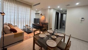 A modern living room with a sofa, a coffee table, and a dining area set for four with plates and glasses. - Luxury 1-bedroom fully furnished Lifeline apartment  (Abu Dhabi)