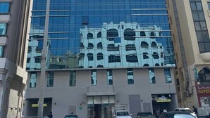 A tall, modern building with a reflective glass facade, surrounded by other buildings. - Luxury 1-bedroom fully furnished Lifeline apartment  (Abu Dhabi)