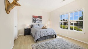 A bedroom with a bed, a mounted deer head, a painting, a window, and a rug.