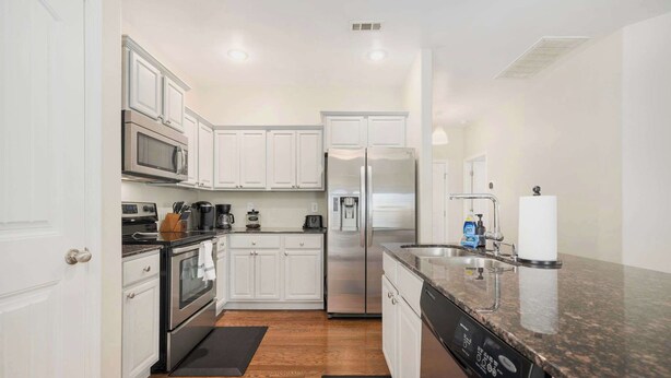 A kitchen with white cabinets, stainless steel appliances, a dishwasher, and a granite countertop.