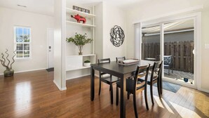 A dining area with a dark wooden table and chairs, white shelving with decorative items, and a sliding glass door leading to an outdoor patio.