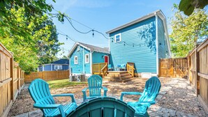 Patio con una casa azul, terraza de madera y sillas Adirondack.