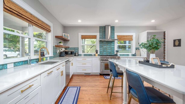 Una cocina moderna con armarios blancos, una isla central con taburetes y un amplio ventanal que proporciona luz natural.