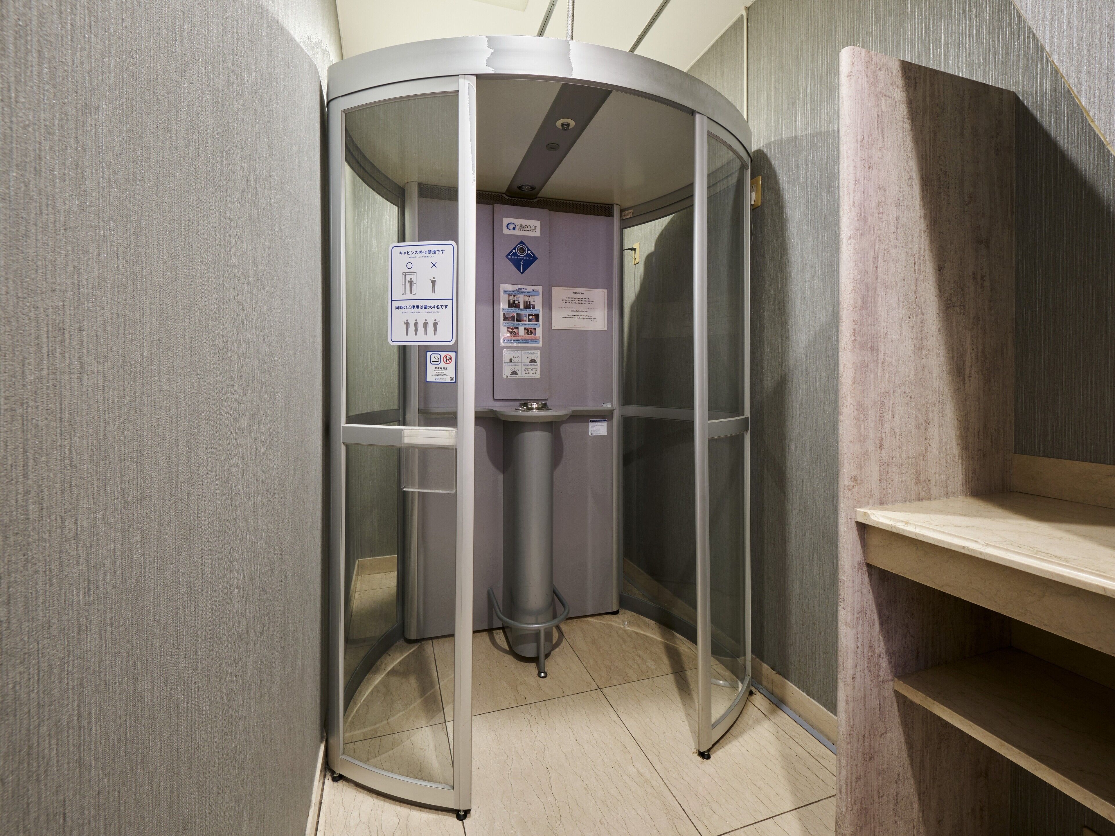 A compact, modern elevator with a glass door, a control panel with various buttons, and a small trash bin.