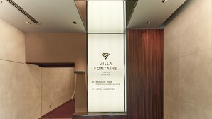 Un pasillo moderno de hotel con una recepción, un logotipo y un cartel que indica el nombre y la ubicación del hotel.