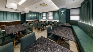 Un restaurante moderno con mesas de mármol, asientos tapizados en verde e iluminación empotrada.