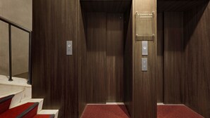 Un ascensor moderno con paneles de madera y una placa metálica que indica que pertenece al Bangkok Bank.