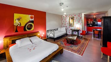 Un dormitorio con cama, mesitas de noche, escritorio, silla, sofá rojo, sillón rojo, alfombra roja, pared roja, lámpara de techo roja, espejo con marco rojo, cuadro con marco rojo y zona de cocina con detalles en rojo.