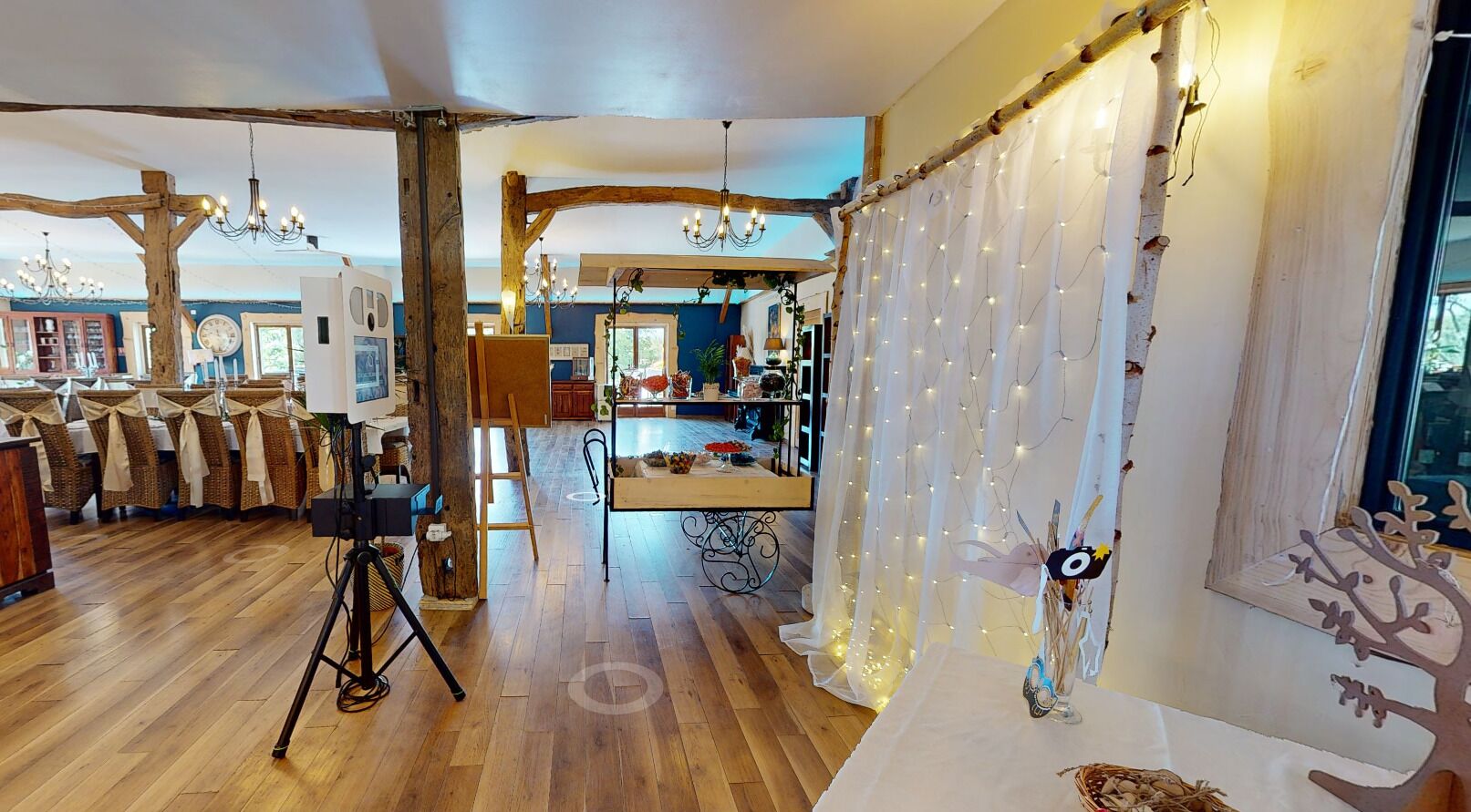 Un intérieur rustique avec des planchers en bois, un coin repas doté d’une longue table et un rideau décoratif agrémenté de guirlandes lumineuses.