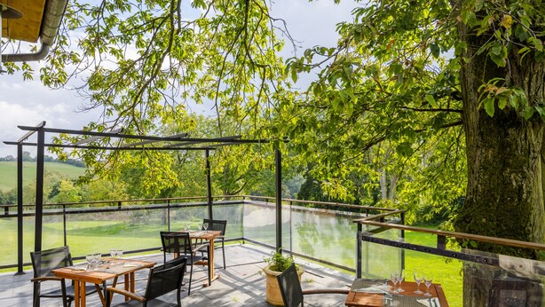 Un patio al aire libre con mesas y sillas, con vistas a un paisaje verde exuberante.
