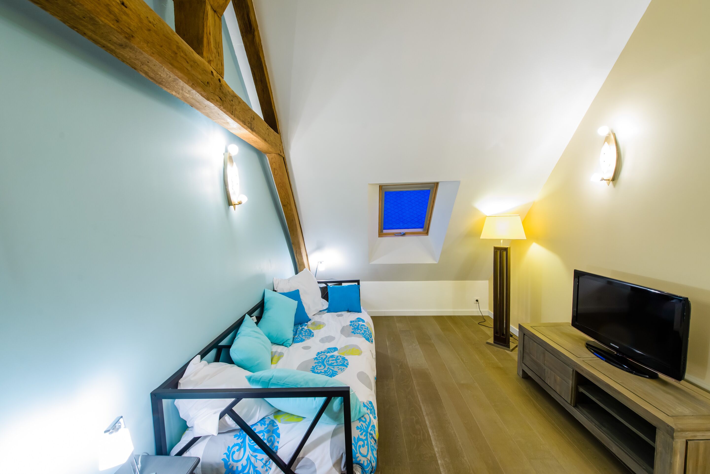 A bedroom with a bed, a TV, a lamp, and a small window.