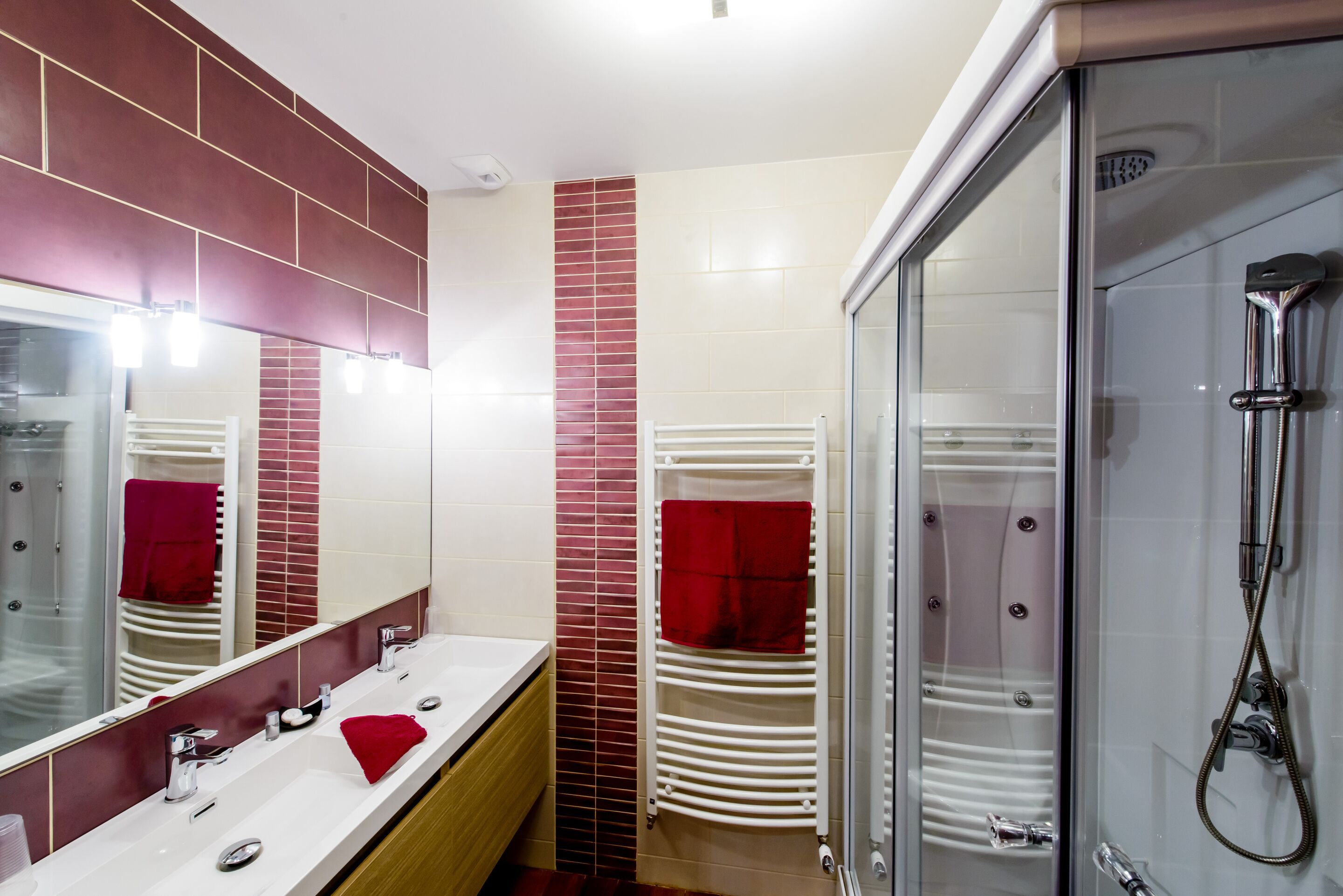 A modern bathroom with a large mirror, two sinks, a glass shower enclosure, and a towel rack.