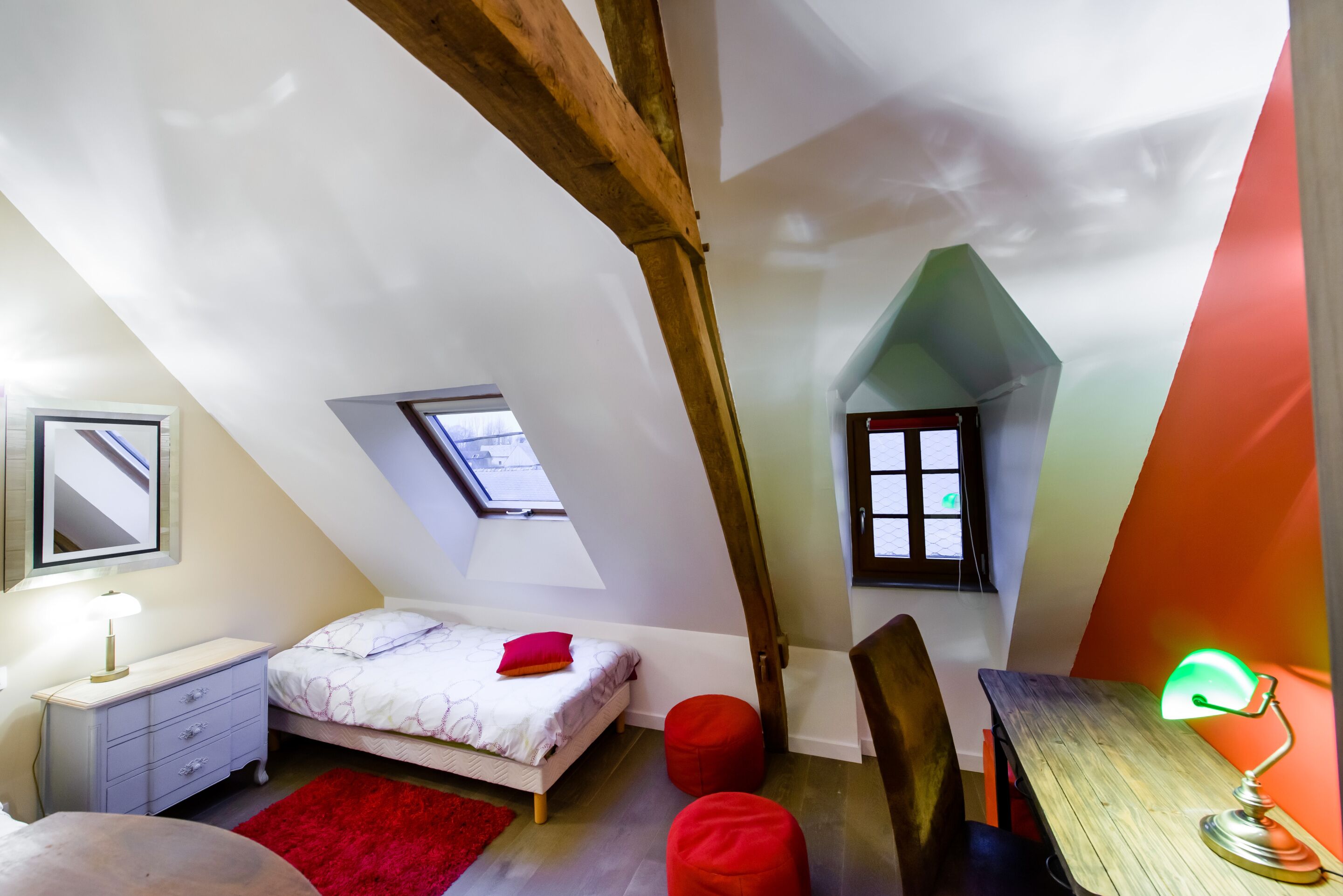 Une chambre avec un plafond en pente, un lit, un bureau et deux fenêtres.