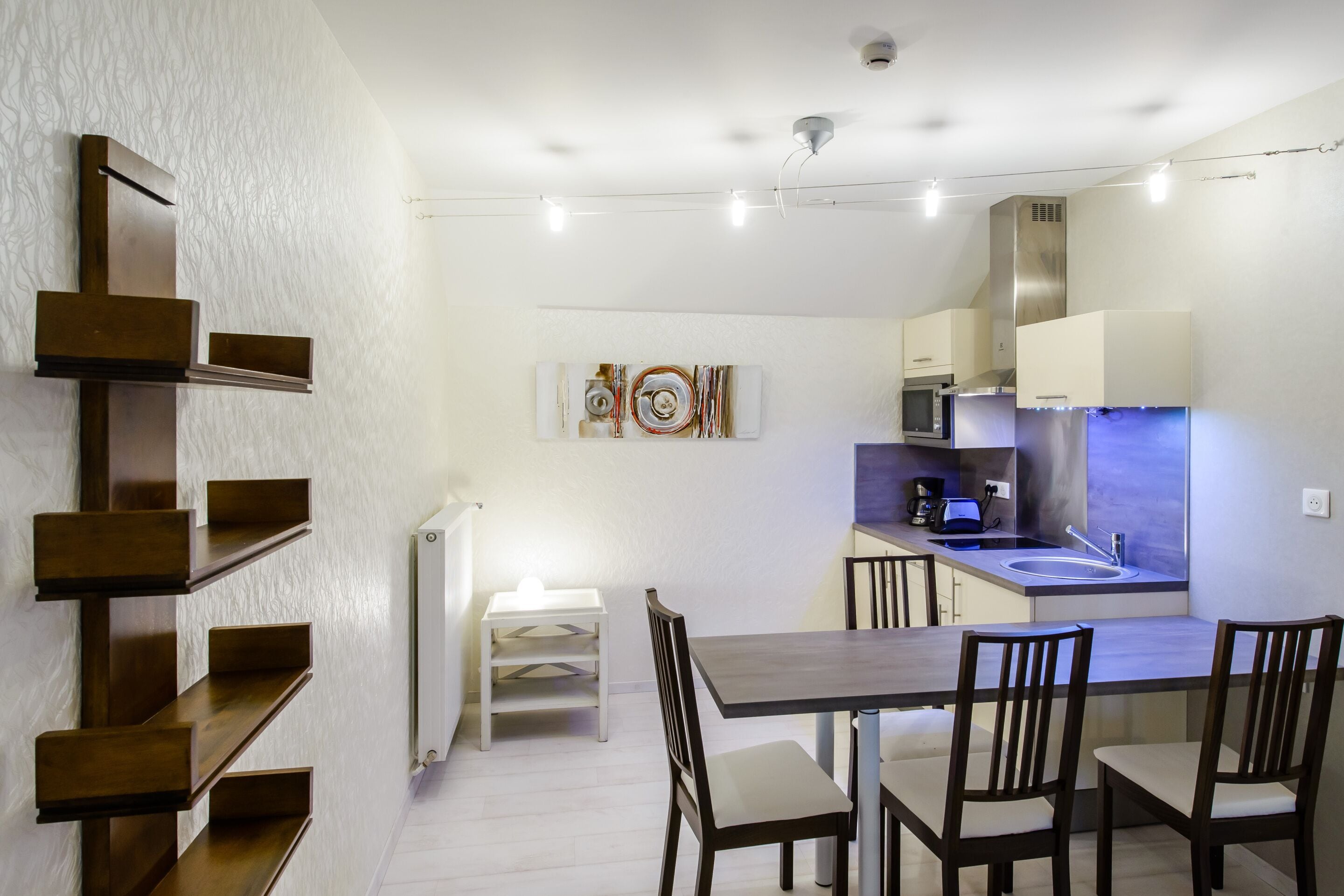 A modern kitchen with a dining area, white walls, and a hanging light fixture.