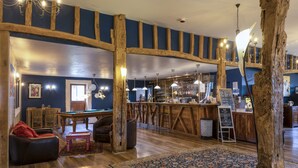 Zona de bar con vigas de madera, mesa de billar y mostrador con taburetes.