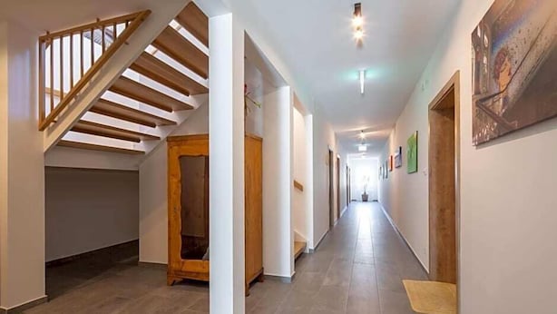 A hallway with a wooden staircase, white columns, and a tiled floor.