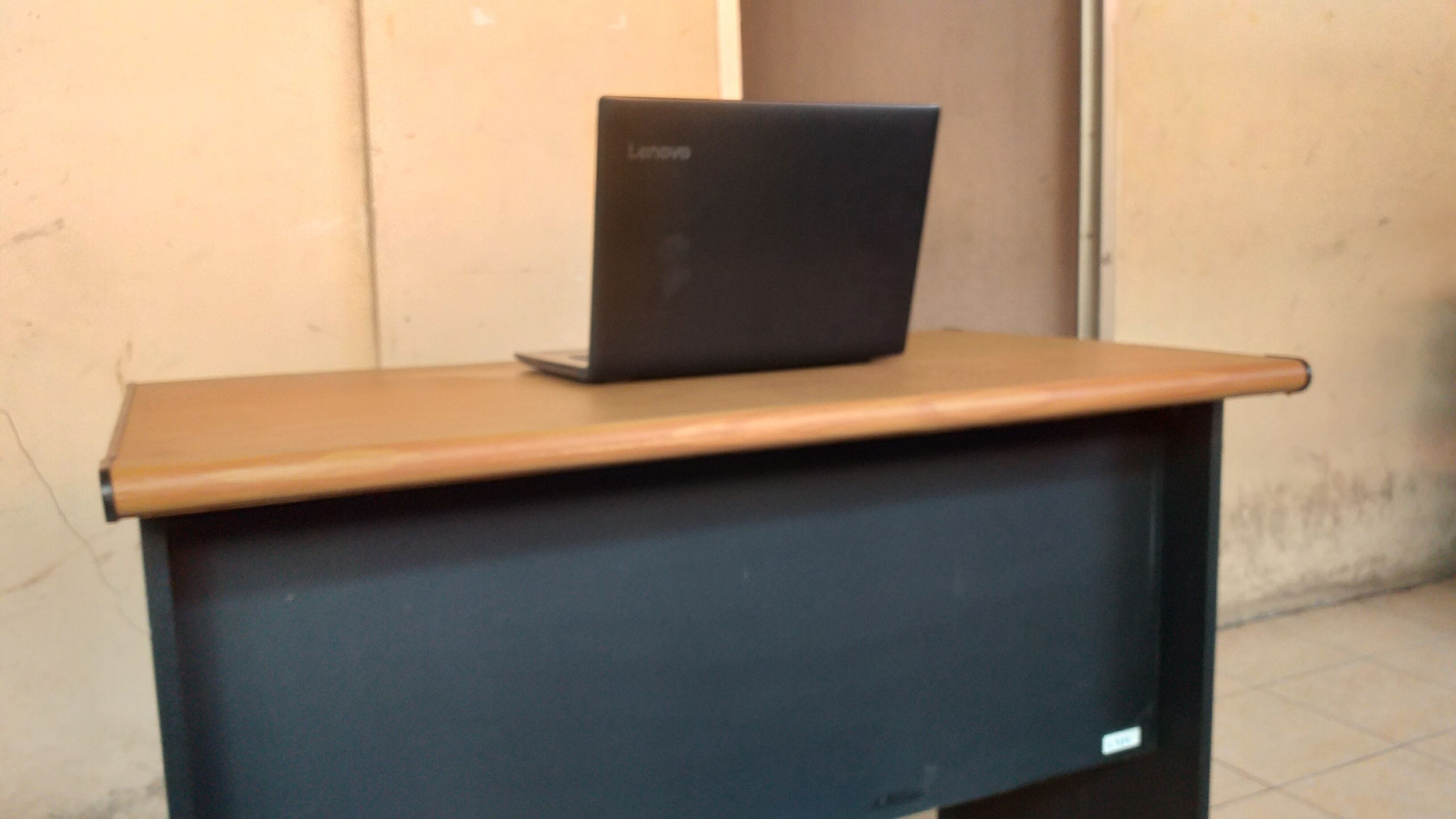 A laptop on a desk with a dark surface and a brown top.