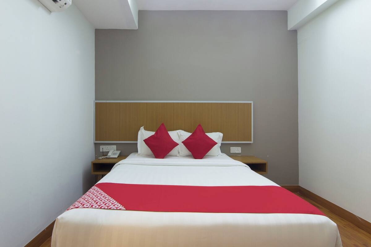 A hotel room with a bed, a nightstand, a telephone, and a wall-mounted shelf.