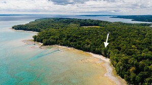 Luchtbeeld van een kustgebied met een strand, dicht bos en een groot wateroppervlak.