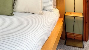 Um quarto com cama, almofadas, mesa de cabeceira, abajur e quadros na parede.