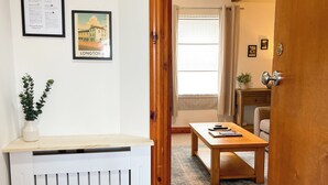 Quarto com radiador branco, porta de madeira, placa de boas-vindas emoldurada e quadro de um edifício.