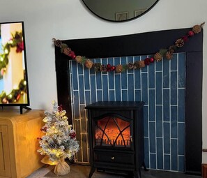 A fireplace with a decorative garland, a small Christmas tree with lights, and a television on a wooden cabinet. - Borders Retreat, Cosy 1 Bed Flat - near M6 Jct45, A75, Gretna & Carlisle (Longtown)