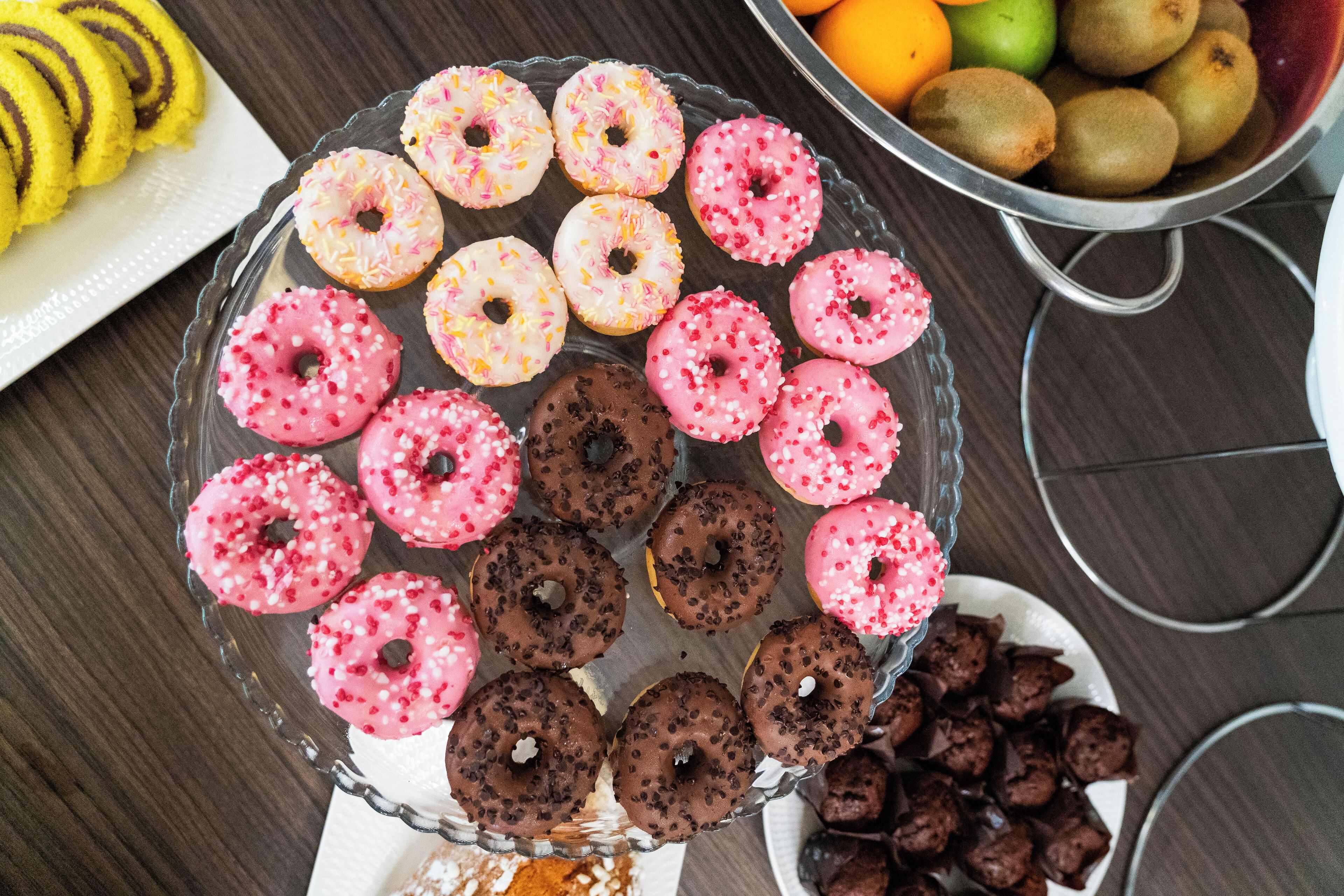 A glass plate with assorted donuts and a bowl of fruit.