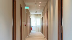 Een lange, smalle hotelgangen met deuren aan weerszijden, een vloerbedekking en een plafond met ingebouwde verlichting.