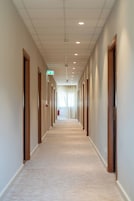 Un lungo e stretto corridoio d'albergo con porte su entrambi i lati, pavimento rivestito di moquette e soffitto con faretti.