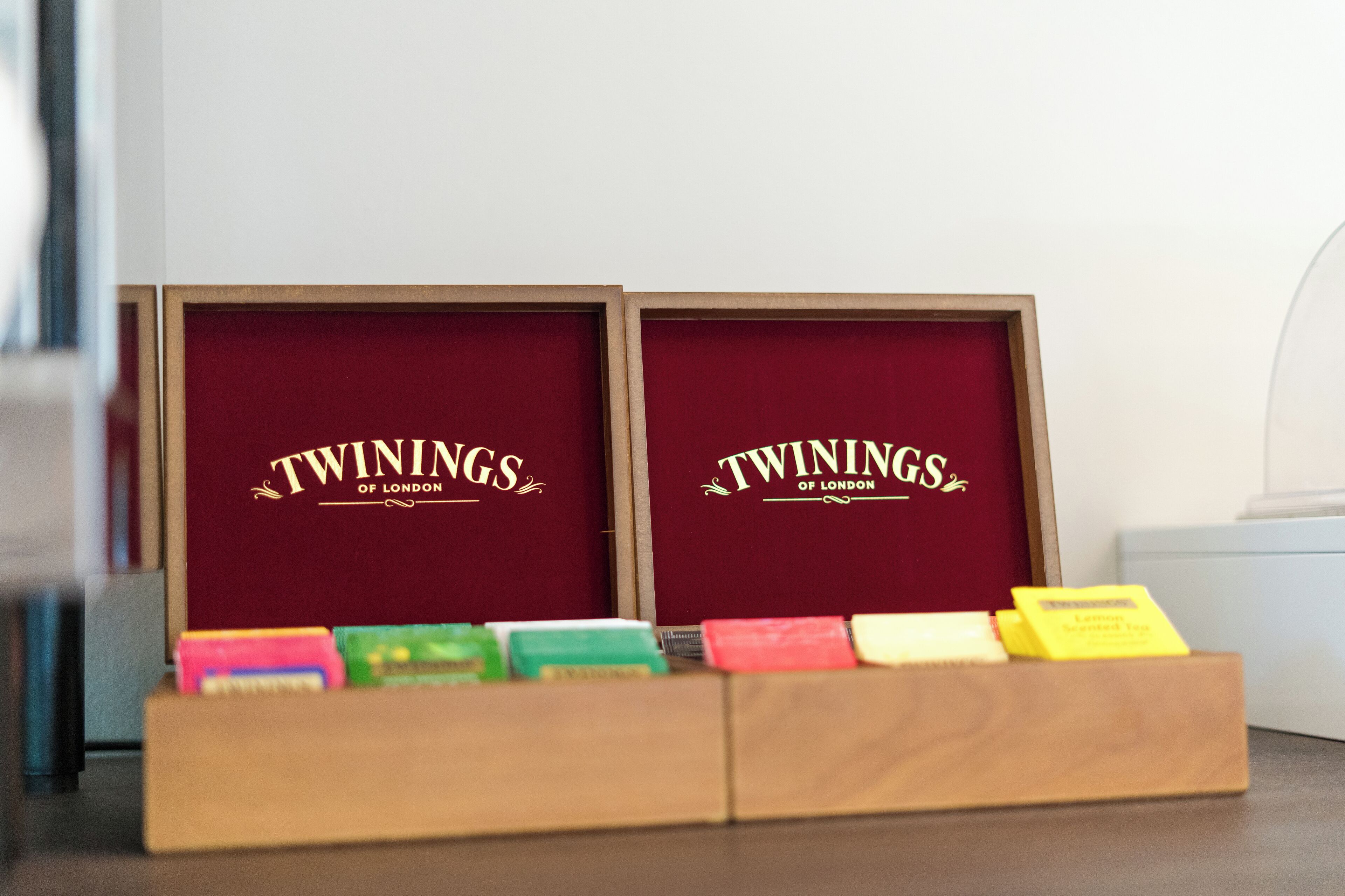 Two wooden display cases with the text 'TWININGS OF LONDON' on a red interior. In front, there are several colorful boxes, possibly containing products.