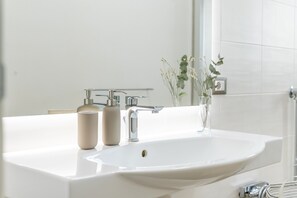 Un baño con un lavabo blanco, dos botellas beige, un espejo y una planta.