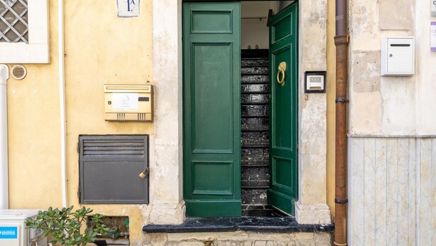 A green door with a brass handle, a mailbox, and a small window with a metal grille. - Vico21 Apartment in Central Modica with Balcony, Wi-Fi, and Air Conditioning (Modica)