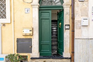 Une porte verte avec une poignée en laiton, une boîte aux lettres et une petite fenêtre ornée d’une grille métallique.