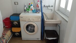 A compact laundry room with a washing machine, a sink, and various cleaning supplies. - Vico21 Apartment in Central Modica with Balcony, Wi-Fi, and Air Conditioning (Modica)