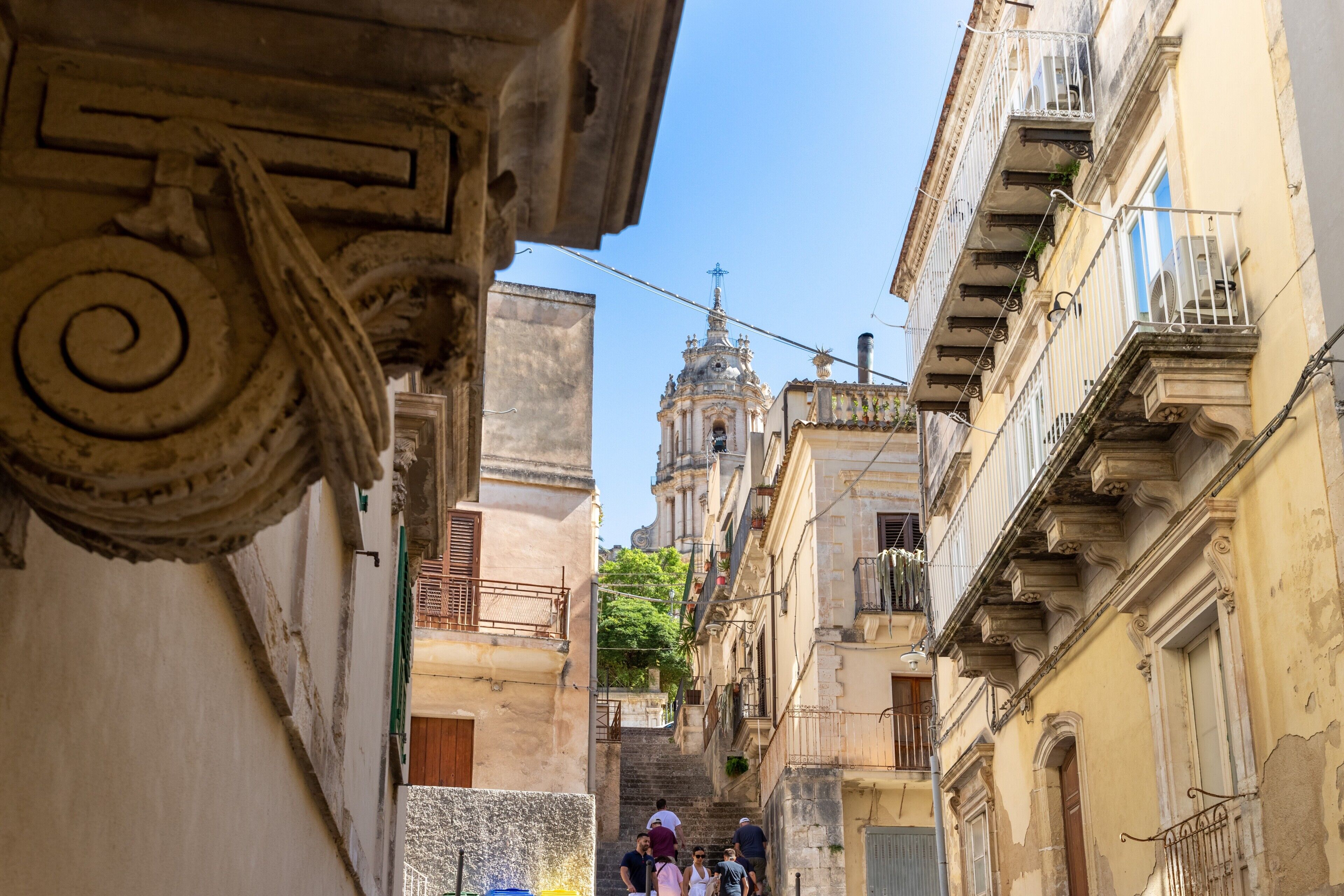 A narrow street with historic buildings, a bell tower, and a staircase leading to a higher level.