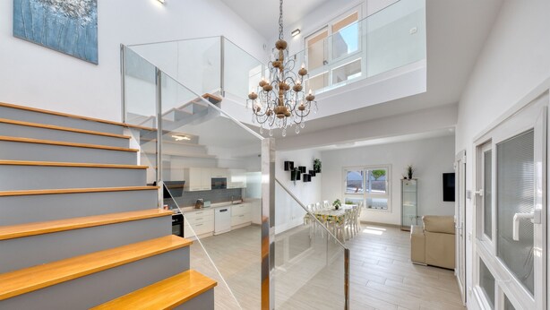 A modern interior with a staircase, a chandelier, a dining area, and a kitchen.