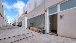 A modern residential building with a narrow street, potted plants, and a clear sky.