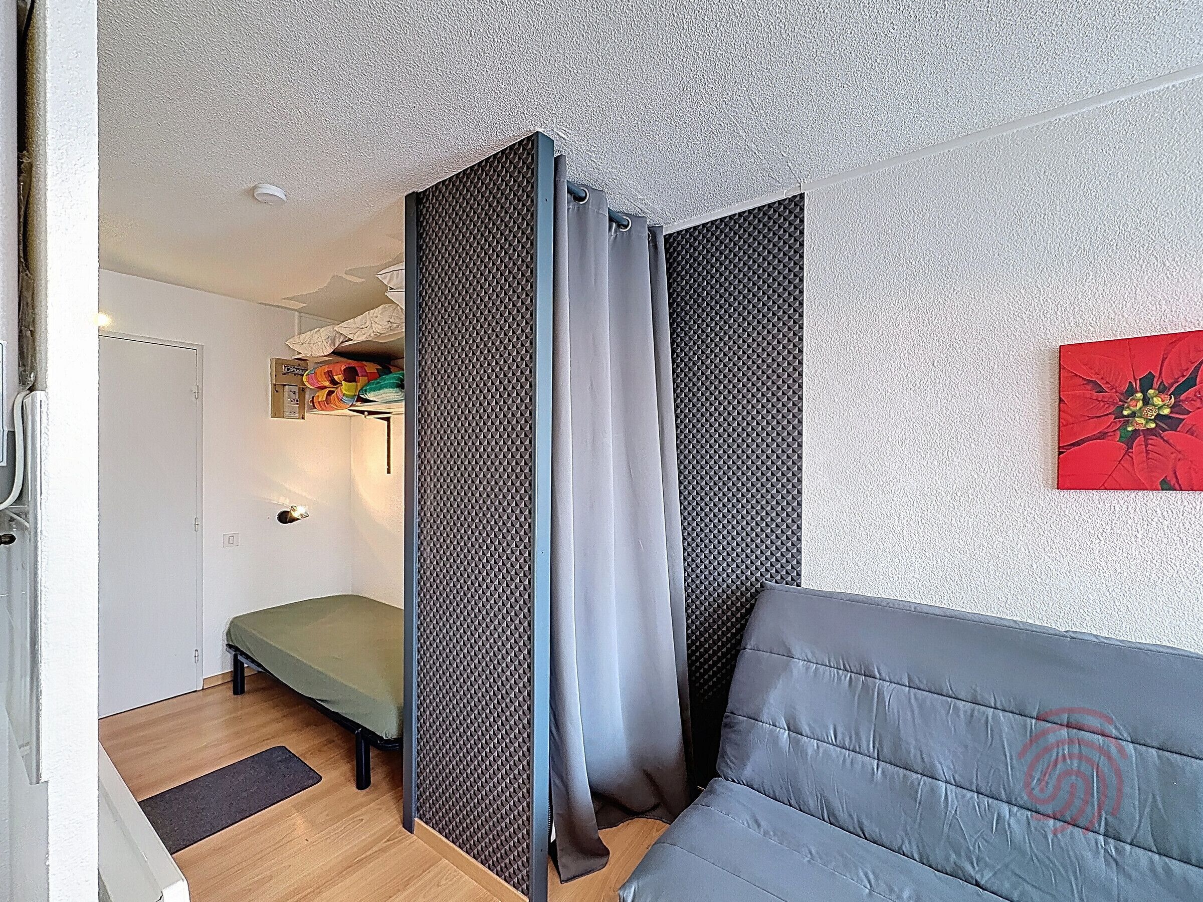 Une pièce comprenant un canapé gris, un lit, un panneau de séparation à motifs, une porte et une œuvre d’art accrochée au mur.