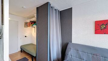 Une pièce comprenant un canapé gris, un lit, un panneau de séparation à motifs, une porte et une œuvre d’art accrochée au mur.