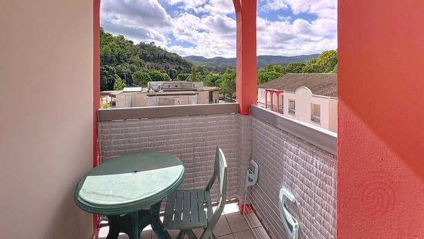 Ein Balkon mit Tisch und Stühlen, eine rote Wand und Blick auf eine hügelige Landschaft.