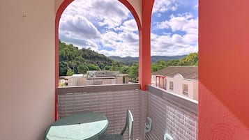Un balcon avec une table et des chaises, un mur rouge et une vue sur un paysage vallonné.