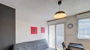 Ein modernes Wohnzimmer mit einem grauen Sofa, einer Deckenleuchte, einer Wanduhr und einem Fenster mit Blick.