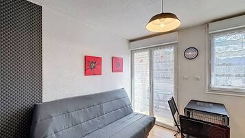 Un salon moderne avec un canapé gris, un luminaire au plafond, une horloge murale et une fenêtre donnant sur un beau paysage.