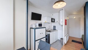 Eine kompakte Küche mit Mikrowelle, Toaster und Spüle, einem flachbildschirmfernseher über der Arbeitsfläche und einem kleinen Kühlschrank.