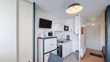 Une cuisine compacte équipée d’un four à micro-ondes, d’un grille-pain et d’un évier, d’un téléviseur à écran plat fixé au-dessus du comptoir et d’un petit réfrigérateur.